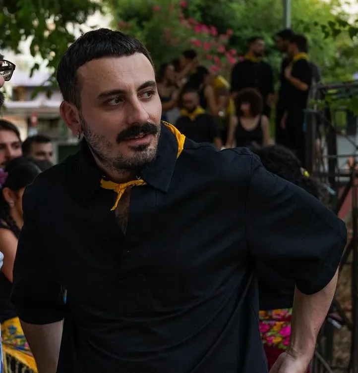Ο Παναγιώτης Λιαρόπουλος με μαύρο πουκάμισο και κίτρινο μαντήλι στον λαιμό, σε υπαίθρια γιορτή